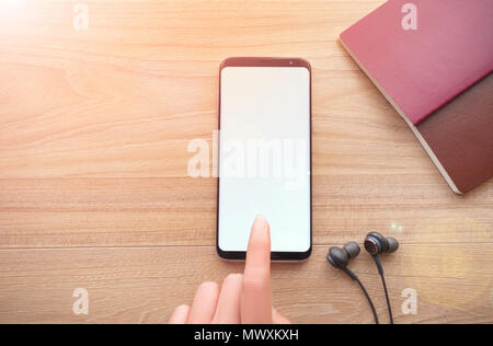 Technologiekonzept, Frau Hand smartphone Holding auf Holz Tisch mit schwarzem Kopfhörerkabel Hintergrund, Ansicht von oben. Stockfoto