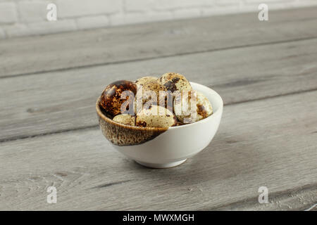 Gefleckte Wachteleier in kleinen Porzellan Schüssel auf grau Holzschreibtisch. Stockfoto