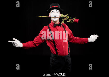 Mime-Holding rote Rose im Mund und stehen mit offenen Armen isoliert auf Schwarz Stockfoto