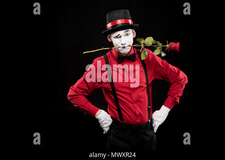 Mime Grimassen und halten rote Rose im Mund auf Schwarz isoliert Stockfoto