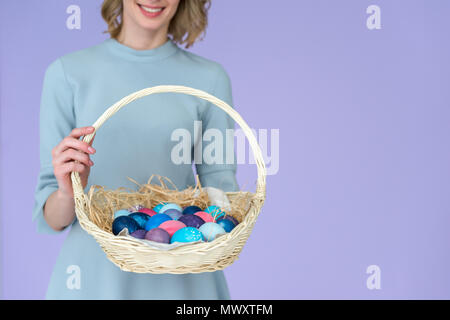 Nahaufnahme der Frau mit bemalten Eiern zu Ostern Korb gefärbten Eiern auf Violett isoliert Stockfoto