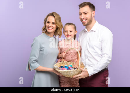 Lächelnd Familie holding Korb mit Ostereiern isoliert auf Violett Stockfoto