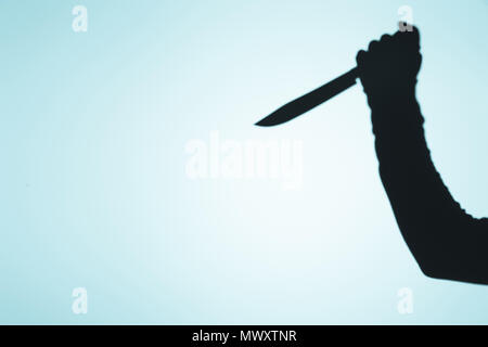 Gespenstische Schatten der Person, die Messer in der Hand auf Blau Stockfoto