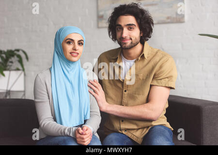Muslimische Paare sitzen auf dem Sofa und in der Kamera zu Hause suchen Stockfoto