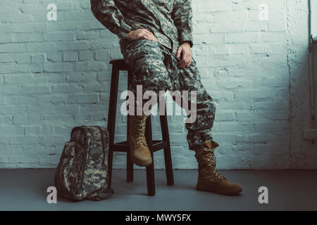 Teilweise mit Blick auf die Soldaten in Uniform sitzen auf Stuhl gegen weiße Wand Stockfoto