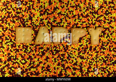 Glücklich. Das Wort von den essbaren cracker Buchstaben liegt auf der verglasten Pulver. Eine große Anzahl von süßen, bunten Perlen von sehr kleinen Größe für die Dekoration o Stockfoto