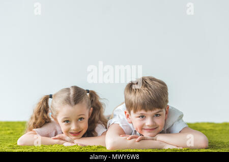 Gerne kleine Kinder liegen auf Rasen und lächelnd an der Kamera auf Grau Stockfoto