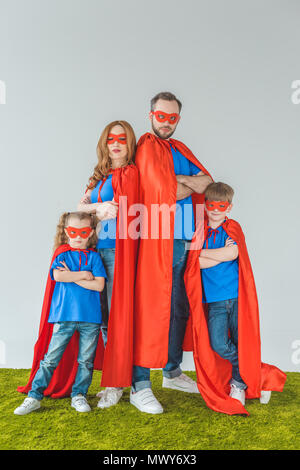 Familie in Superhelden Kostüme Stehen mit verschränkten Armen und Kamera auf Grau Stockfoto