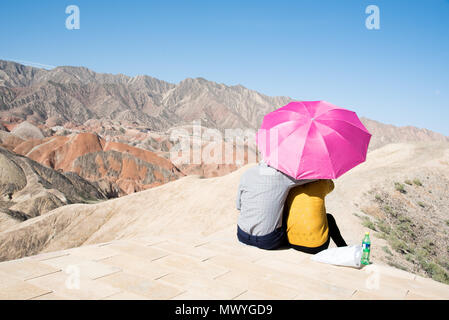 Paar genießt die Aussicht durch einen Regenschirm bei Zhangye-Danxia - Geopark, Provinz Gansu, China geschützt Stockfoto