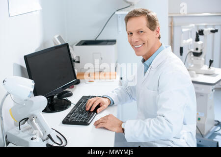 Schöner Lächeln männlichen Augenarzt arbeiten mit Computer in der Klinik Stockfoto