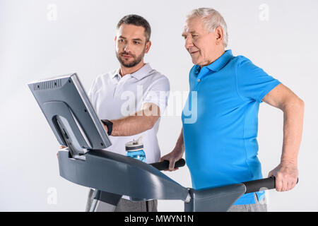 Rehabilitation Therapeuten Unterstützung älterer Mann Ausübung auf Laufband isoliert auf Grau Stockfoto