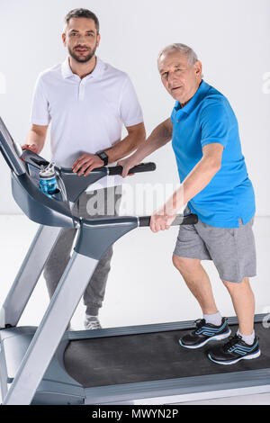 Rehabilitation Therapeut und älterer Mann auf Laufband isoliert auf Grau Stockfoto