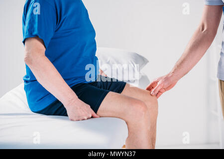 7/8 shot der Rehabilitation Therapeut prüfen Senior mans Knie auf Massage Tisch Stockfoto