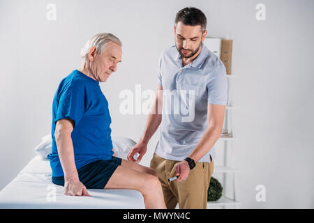 Rehabilitation Therapeut mit reflexhammer Überprüfung älterer mans Knie auf Massage Tisch Stockfoto