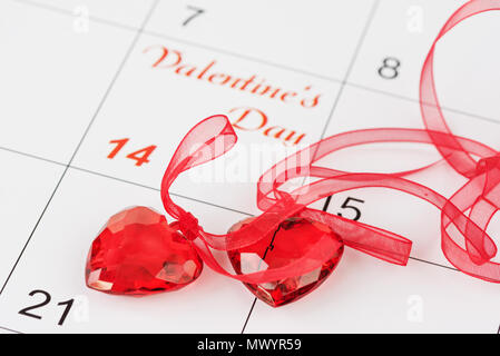 Zwei transparente rote Herzen mit roten Bändern auf dem Kalender mit der Aufschrift Valentinstag. Hintergrund für eine Grußkarte für Saint Valenti Stockfoto