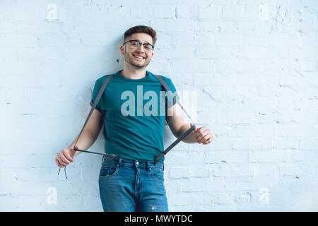 Lächelnd bärtigen Mann in Jeans mit Hosenträgern vor der Mauer Stockfoto