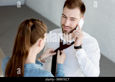 Frau mit Krawatte auf Mann, während er auf dem Smartphone Stockfoto
