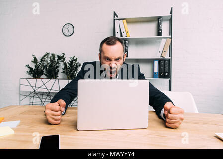 Portrait von gestressten Geschäftsmann im Anzug am Arbeitsplatz schreiend mit Laptop im Büro Stockfoto