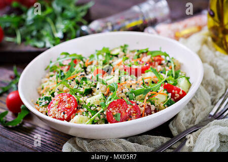 Salate mit Quinoa, Rucola, Rettich, Tomaten und Gurke in Schüssel auf Holz- Hintergrund. Gesunde Lebensmittel, Ernährung, Entgiftung und vegetarische Konzept. Stockfoto