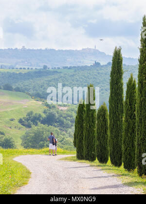 San Quirico d'Orcia, Italien, 10. Mai 2018; zwei Männer eine Drohne über toskanische Landschaft fliegen. Reihe von Zypressen. Stadt Pienza sichtbar in weiter Ferne. Stockfoto