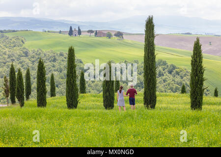 San Quirico d'Orcia, Toskana, Italien; 10. Mai 2018; junge Erwachsene touristische Paar Ansehen unter Zypressen. Der Mensch ist ein Foto des Vitaleta Kapelle Stockfoto