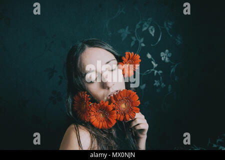 Ein Mädchen mit blauen Augen und langen Haaren selbst Abdecken mit einer gerbera Blume Stockfoto