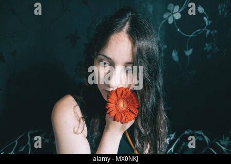 Ein Mädchen mit blauen Augen und langen Haaren selbst Abdecken mit einer gerbera Blume Stockfoto