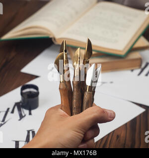 Kalligraphie Handschrift Zubehör, style Füllfederhalter nib-Sammlung in der Hand, abstrakte Papier und Holz- Hintergrund. Farben Foto Stockfoto