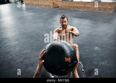 Passen junge Mann in Sportkleidung mit einem weiblichen Partner auf einen Fitnessraum, Arbeiten mit einem medizinball während einer Trainingseinheit Stockfoto