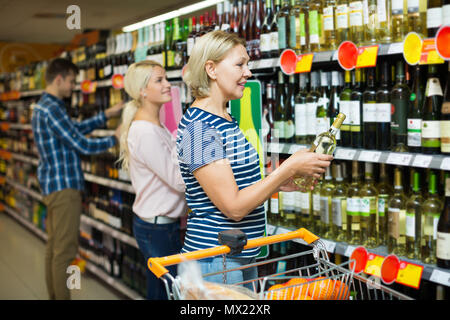 Lächelnd reife blonde Frau kaufen Flasche Wein im Supermarkt Stockfoto