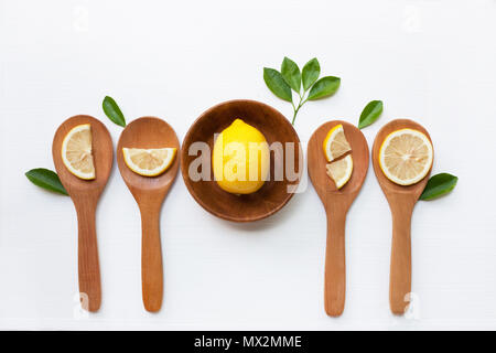 Zitrone auf hölzerne Schüssel und Zitronenscheiben auf Holzlöffel mit Blatt auf weißem Hintergrund, Ansicht von oben Stockfoto