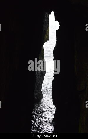 Eine Lücke in einer Höhle am Rande des Meeres lassen Licht in den dunklen Bereich. Stockfoto