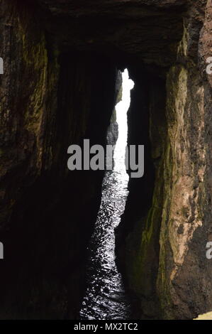 Eine Lücke in einer Höhle am Rande des Meeres lassen Licht in den dunklen Bereich. Stockfoto