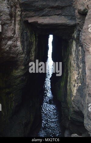 Eine Lücke in einer Höhle am Rande des Meeres lassen Licht in den dunklen Bereich. Stockfoto