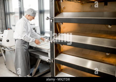 Baker rollt Teig bei der Herstellung Stockfoto