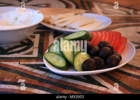 Oliven und in Scheiben geschnittene Gurken und Tomaten Platte aus einem traditionelle libanesische Frühstück mit labneh und Käse im Hintergrund. Stockfoto