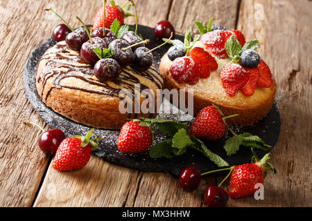 Natürliche organische Kuchen mit Schokolade, Puderzucker, Minze, Erdbeeren, Kirschen und Heidelbeeren in der Nähe eingerichtet - bis auf einer Schiefertafel board. Horizontale Stockfoto