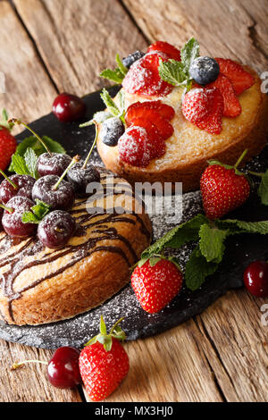 Frisch gebackene zwei Kuchen mit Schokolade, Minze, Erdbeere, Kirsche, Heidelbeere close-up auf dem Tisch. Vertikale Stockfoto