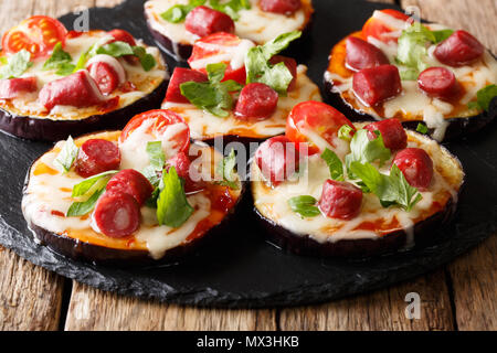 Mini Pizza aus Auberginen mit Mozzarella, Tomaten, Wurst und grünen Close-up auf dem Tisch. Horizontale Stockfoto