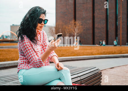 Glücklich und junge schöne Frau verwendet das Telefon. Süße Mädchen prüft, SMS, E-Mail outdoor. Konzept der Lifestyle, Lebensfreude. Weibliche genießt online einkaufen. Stockfoto