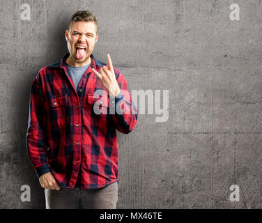 Jungen gutaussehenden Mann, Rock Symbol mit Händen, Schreien und feiern Mit herausgestreckter Zunge Stockfoto