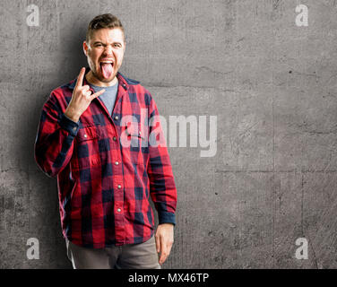 Jungen gutaussehenden Mann, Rock Symbol mit Händen, Schreien und feiern Mit herausgestreckter Zunge Stockfoto