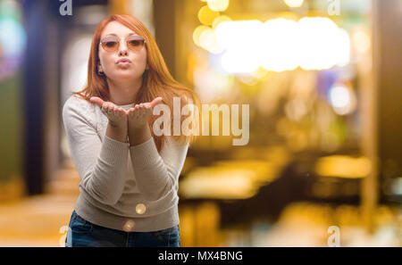 Schöne junge rothaarige Frau, die Liebe zum Ausdruck kommt, bläst Kiss an der Kamera, in der Nacht flirten Stockfoto