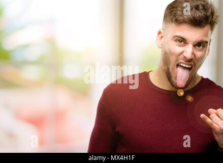 Hübscher junger Mann, Rock Symbol mit Händen, Schreien und feiern Mit herausgestreckter Zunge Stockfoto