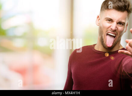 Hübscher junger Mann, Rock Symbol mit Händen, Schreien und feiern Mit herausgestreckter Zunge Stockfoto