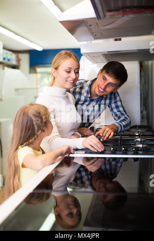 Portrait von lächelnden Familie mit kleinen Tochter Auswahl Küche Herd im Gerät speichern. Fokus auf Frau Stockfoto