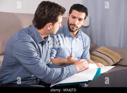 Zwei ernste Männer Arbeiten mit Dokumenten, während auf dem Sofa zu Hause sitzen Stockfoto