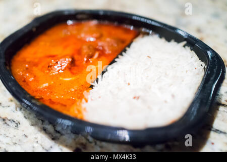 Orange Red Curry Tikka Masala Sauce Makro Nahaufnahme in Kunststoff schwarz tv Dinner fast food gefrorene Mahlzeit Container auf Tabelle mit weißen Basmati Reis Stockfoto