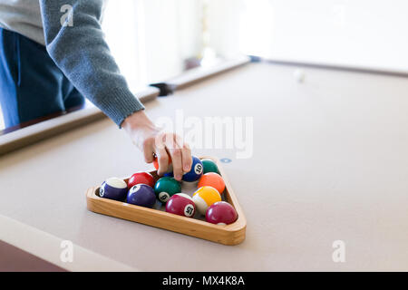 Innenbereich Haus mit Pool Billard Tisch im Wohnzimmer, junger Mann im kalten Winter pullover Inverkehrbringen Kugeln im Inneren Dreieck Rack, Einrichten Spiel Stockfoto