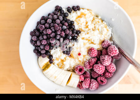 Haferflocken Hafer Reis Pudding porridge bowl Makro Nahaufnahme mit gefrorenen Beeren, Himbeeren, Heidelbeeren, Bananen und Ahorn Sirup Karamell auf Holz- ta Stockfoto